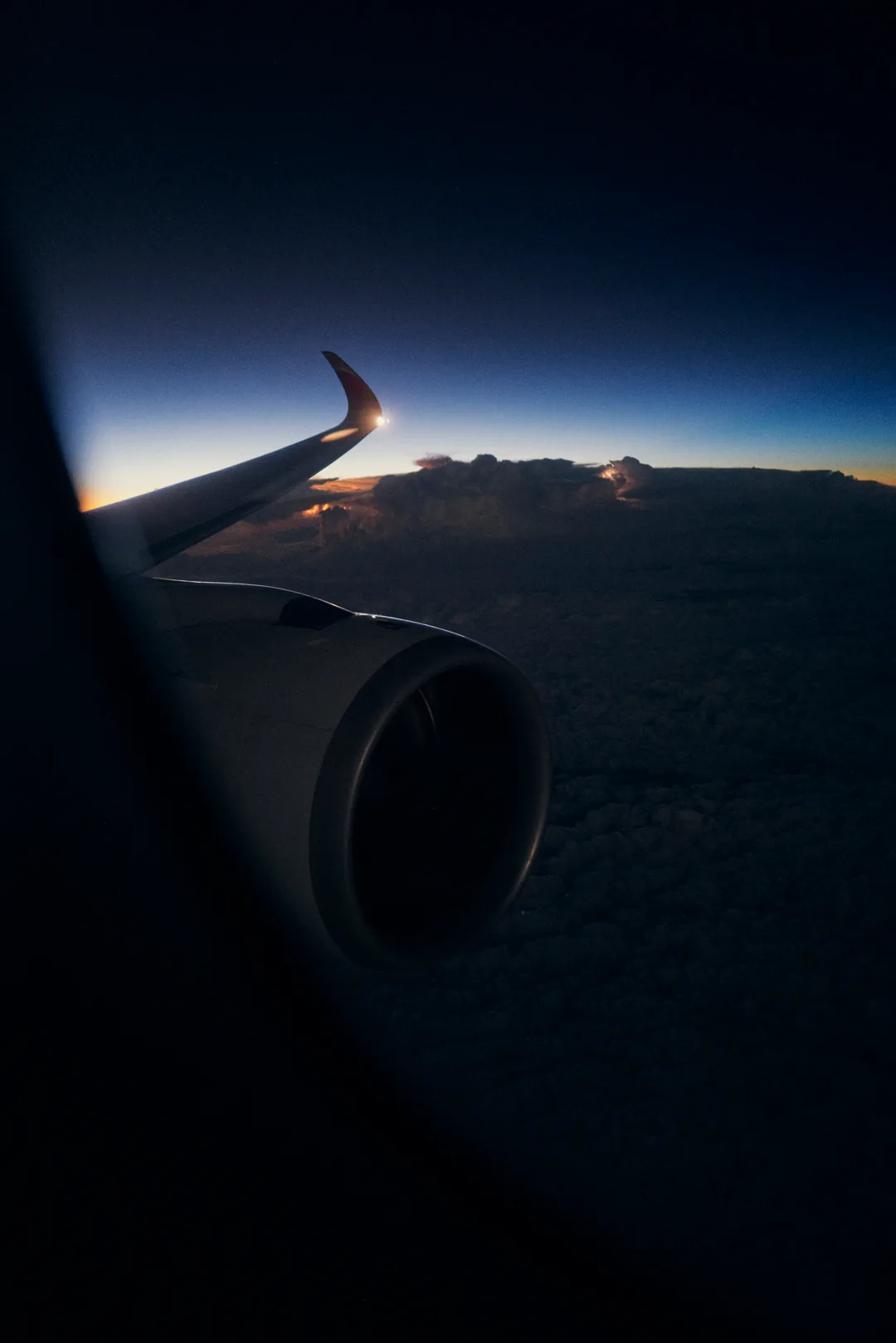 Wing and engine silhouetted against predawn sky, low cloud deck below at FL280, sunrise band on horizon.