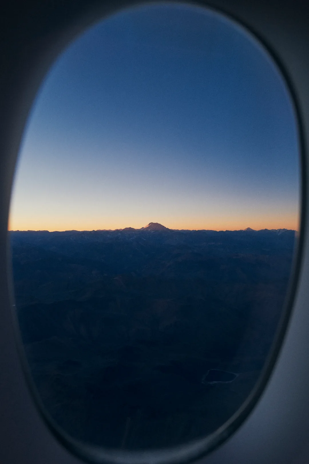 Aconcagua summit catching first light through aircraft window, cordillera below in shadow.
