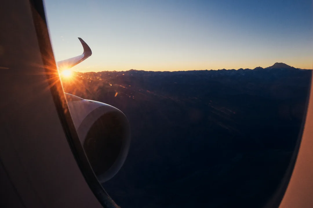 Sunburst off wingtip leading edge with cordillera ridgeline below, distant Aconcagua on horizon.