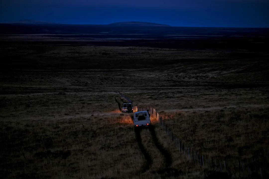 Two white vehicles on a dirt road at dusk, small in a wide plain